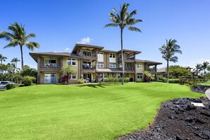 A multi-story hotel with a well-maintained lawn, palm trees, and a clear blue sky. - 🏖️Ground Floor Ocean View Condo Walk to Ocean Club (Waikoloa)