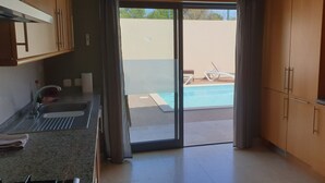 A kitchen with a sink, cabinets, and a view of a pool outside.