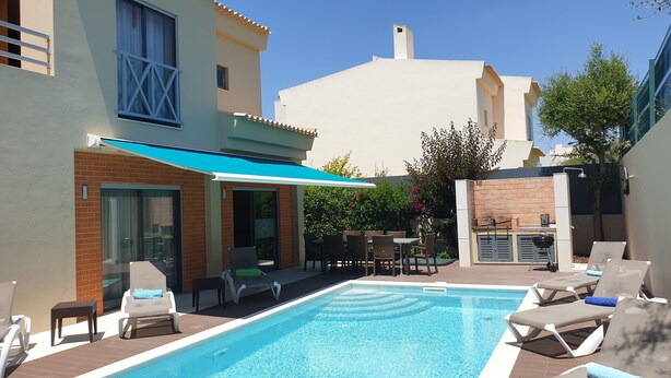 A swimming pool with lounge chairs, a covered patio, and a brick wall.