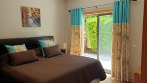 A bedroom with a bed, pillows, a nightstand, a lamp, and a window with curtains.