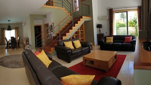 A spacious living room with a staircase, a black leather sofa, a wooden coffee table, and a red rug.