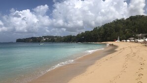 Une plage à l’eau turquoise et limpide, un rivage sablonneux et, en arrière-plan, une colline boisée.