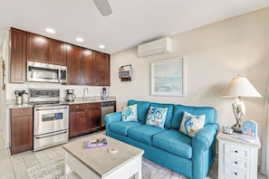 Un espacio habitable compacto con kitchenette, un sofá azul, una mesa de centro y una lámpara.