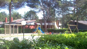 A playground with slides and climbing structures, surrounded by trees and a building with a red roof.
