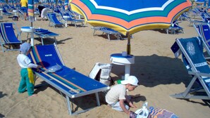 A beach with rows of blue lounge chairs and a colorful umbrella.