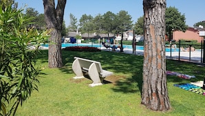 A pool area with a grassy lawn, a bench, and trees.