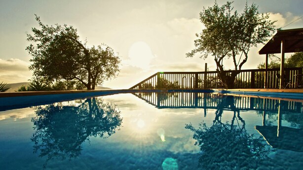 Una piscina con cubierta de madera y barandilla de metal, rodeada de árboles y un cielo despejado.