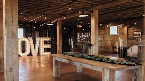 Un intérieur rustique avec des poutres apparentes, un grand panneau lumineux représentant le mot « AMOUR », un banc en bois et des bougies.