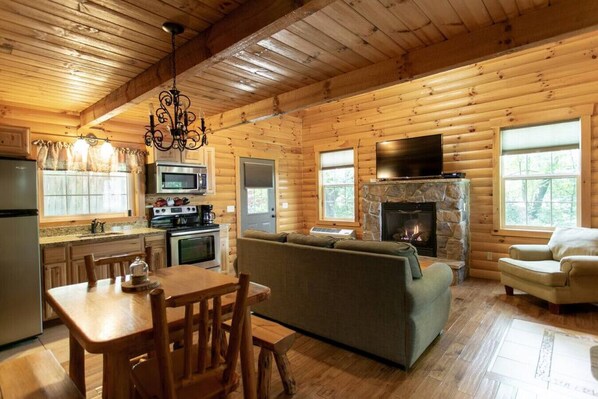 Ein Blockhaus-Interieur mit Küche, Essbereich und Wohnzimmer, ausgestattet mit einem Steinkamin und Holzwänden.