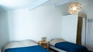 A bedroom with two beds, a wooden nightstand, a hanging light fixture, and a door with a curtain. - abundance, Stone house with land of 2000m2 at the foot of the vercors (La Baume-Cornillane)