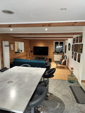 A modern living room with a dining area, wooden walls, a flat-screen TV, and a collection of framed pictures. - abundance, Stone house with land of 2000m2 at the foot of the vercors (La Baume-Cornillane)