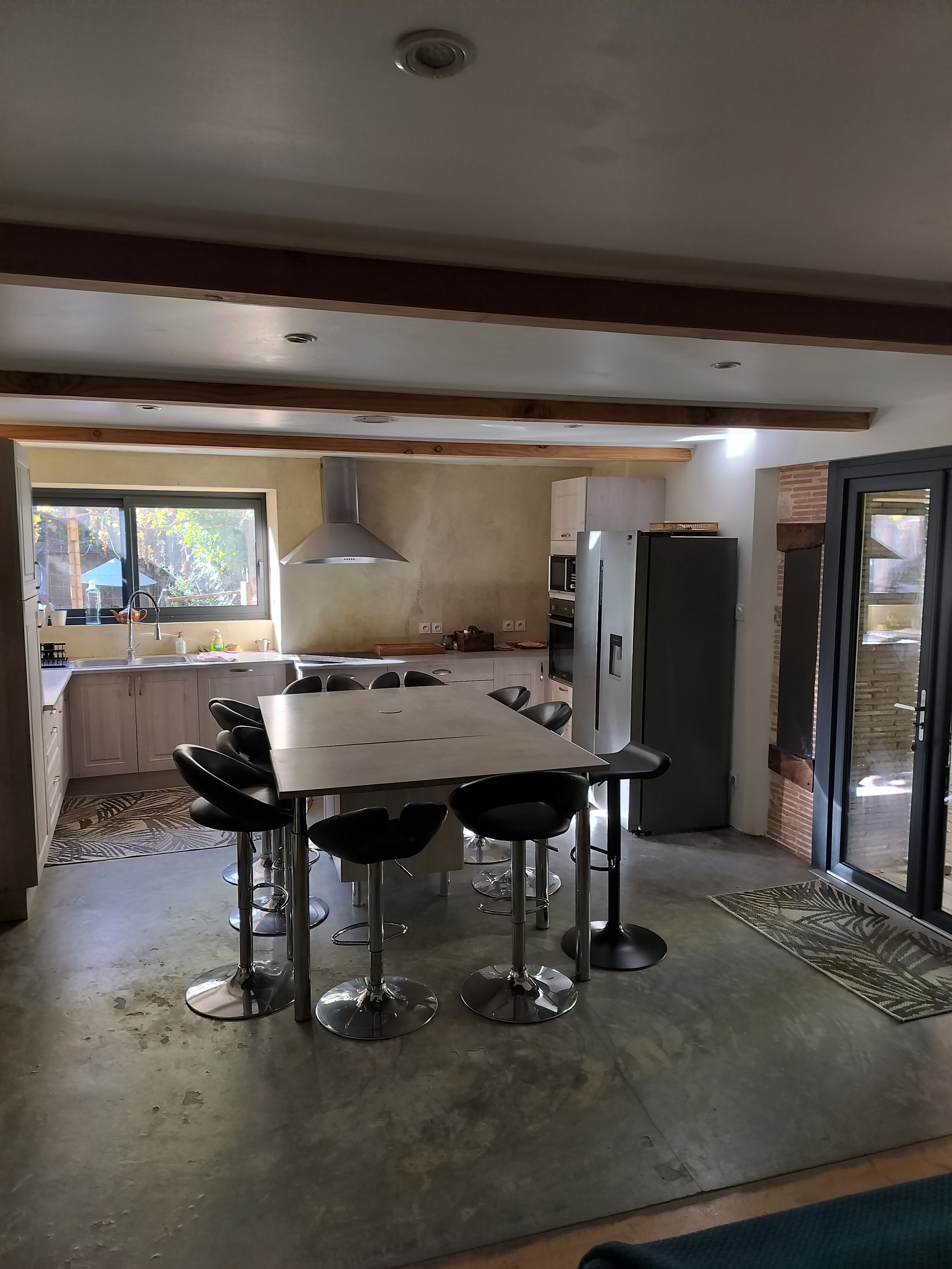 A modern kitchen with a dining area, featuring a large table and bar stools, a built-in oven, and a refrigerator.