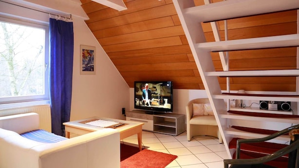 Un salon confortable avec un téléviseur, un canapé, une table et un escalier.