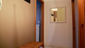 Un couloir étroit avec un banc en bois, une porte dotée d’un miroir et un radiateur.