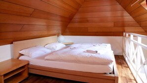 Une chambre avec un plafond en pente en bois, un lit avec une literie blanche, une table de chevet et une commode.
