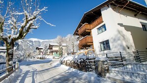 A snow-covered street with buildings, including a hotel with balconies and a wooden fence. - Finest Villa Zell am See - PENTHOUSE, Sauna (Zell am See)
