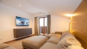 A modern living room with a large sectional sofa, a flat-screen TV mounted on the wall, and a sliding glass door leading to a balcony. - Finest Villa Zell am See - PENTHOUSE, Sauna (Zell am See)