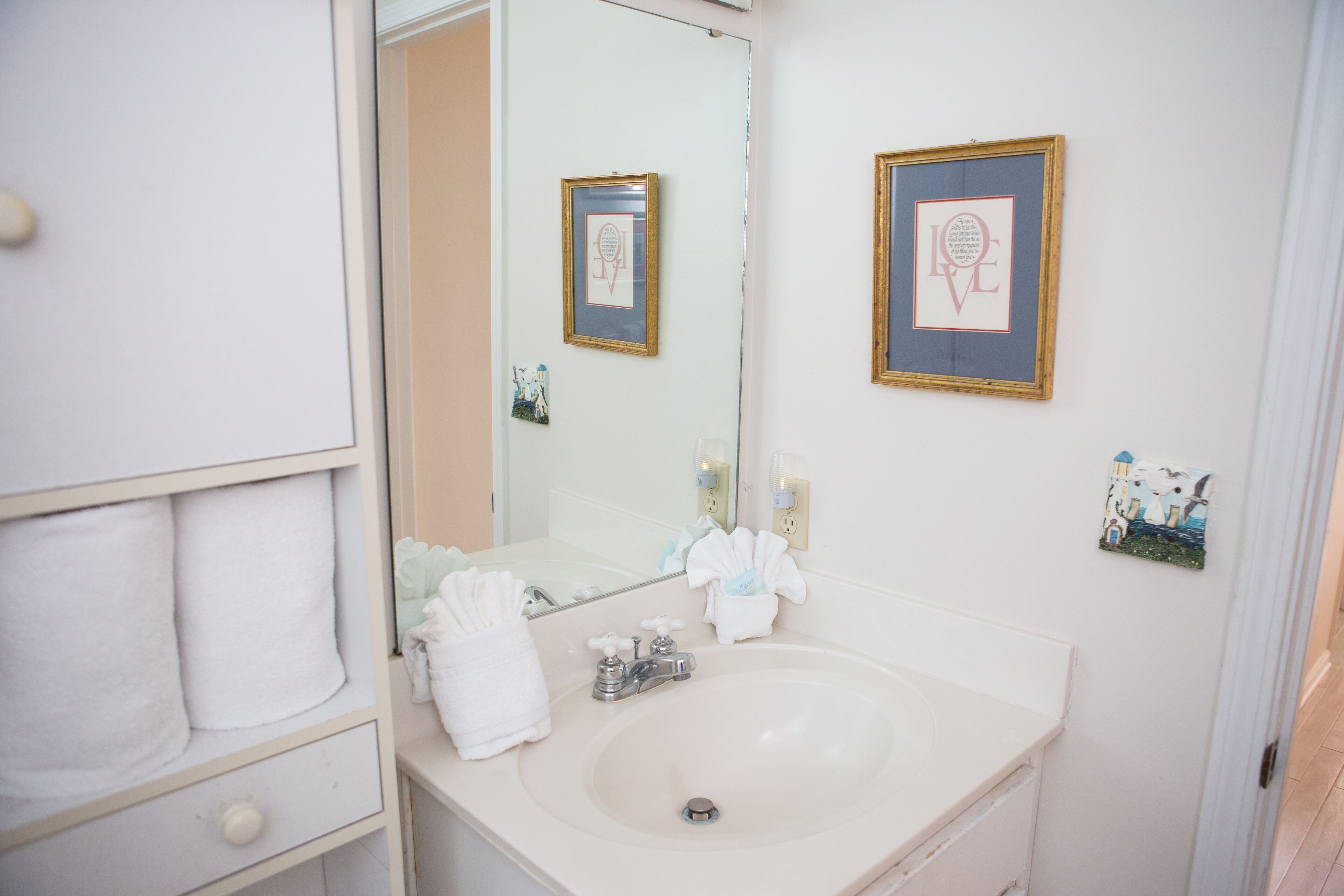 Une salle de bain avec un lavabo, un miroir, des serviettes et des tableaux encadrés accrochés au mur.