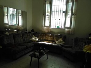 Ein schwach beleuchtetes Wohnzimmer mit einem dunkelgrauen Sofa, einem kleinen Couchtisch und einem Fenster mit Gitterstäben.