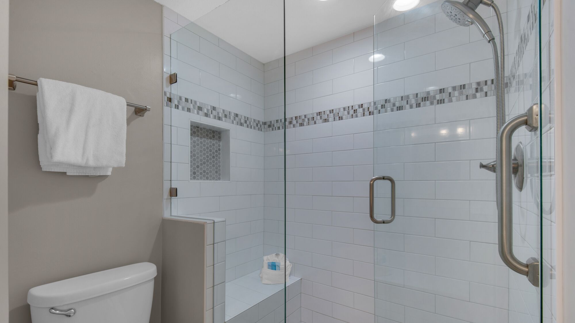 A modern bathroom with a glass-enclosed shower, white tiles, and a toilet.
