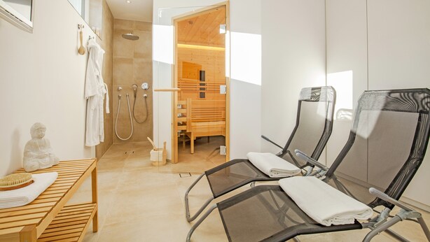 A modern bathroom with a shower, a wooden bench, and two reclining chairs. - Quartier39 (Sankt Johann in Tirol)