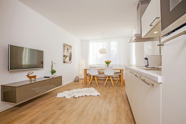 Eine moderne Küche mit Flachbildfernseher, Holzschränken und einer Essecke mit Tisch und Stühlen.