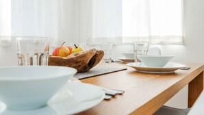A dining table with white plates, bowls, and a wooden bowl containing fruits. - Quartier39 (Sankt Johann in Tirol)