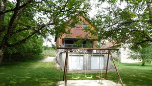 Ein hölzernes Schaukelgestell in einem grünen Garten mit einem rustikalen Gebäude im Hintergrund.