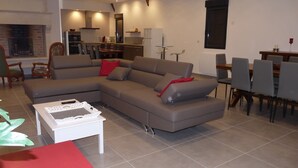 Ein modernes Wohnzimmer mit einem Ecksofa, einem Essbereich mit Tisch und Stühlen und einer Küche im Hintergrund.