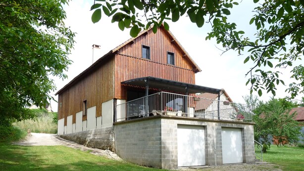 Ein zweistöckiges Holzhaus mit Balkon, Garage und Rasenfläche.