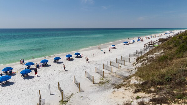 Enjoy the ocean view from the comfort of our beachside location, where umbrellas provide shade and a wooden walkway leads to the water.