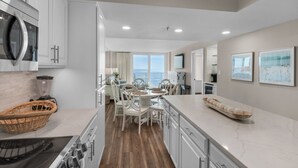 A modern kitchen with white cabinetry, a built-in oven, and a dining area with a view of the ocean.