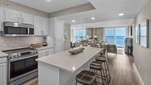 A modern kitchen with stainless steel appliances, a large island with bar stools, and a view of the ocean through large windows.