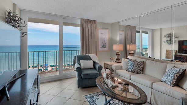 Ein geräumiges Wohnzimmer mit Balkon und Blick auf einen Strand, ausgestattet mit einer Couch, einem Sessel und einem Couchtisch.