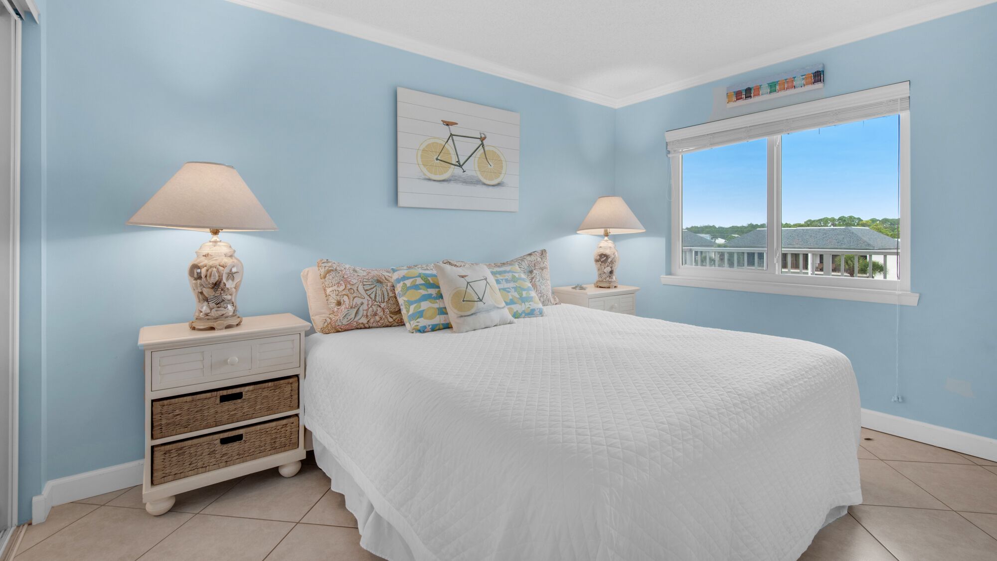 A bedroom with a large bed, two nightstands, wicker baskets, a window with a view, and a ceiling with a light fixture.