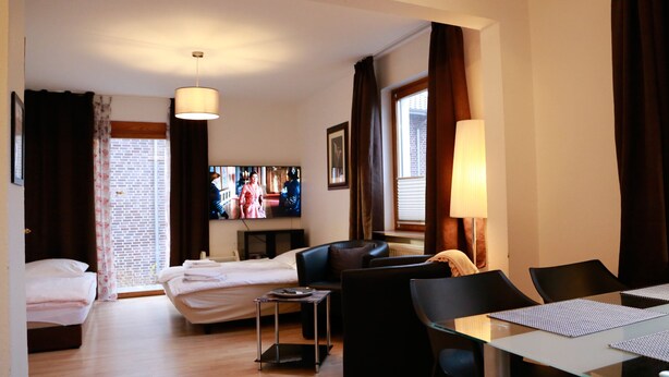 Ett hotellrum med en säng, en soffa, en tv, ett matbord och ett fönster med gardiner.