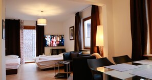 Une chambre d’hôtel avec un lit, un canapé, une télévision, une table à manger et une fenêtre avec des rideaux.