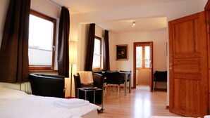 Ett hotellrum med en säng, ett skrivbord och en stol. Det finns en trädörr och ett fönster med gardiner.