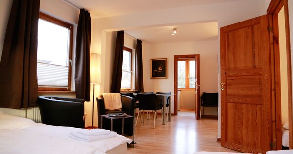 Une chambre d’hôtel avec un lit, un bureau et une chaise. Il y a une porte en bois et une fenêtre avec des rideaux.