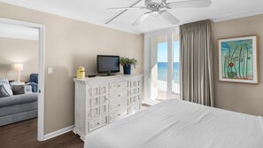 A hotel room with a bed, a dresser with a television, a plant, and a painting. - Gulf-front condo, Private Beach, Pool w/ beach chairs & attraction tickets! (Santa Rosa Beach)