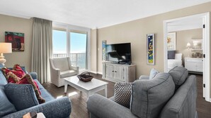 A spacious living room with a balcony, a television, and a dining area. - Gulf-front condo, Private Beach, Pool w/ beach chairs & attraction tickets! (Santa Rosa Beach)