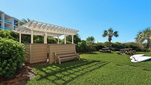 A well-maintained outdoor area with a wooden pergola, a bench, picnic tables, and a surfboard. - 2BR Gulf-Front w/ Private Beach Access, Beach Setup, Pool + Free Tickets! (Santa Rosa Beach)