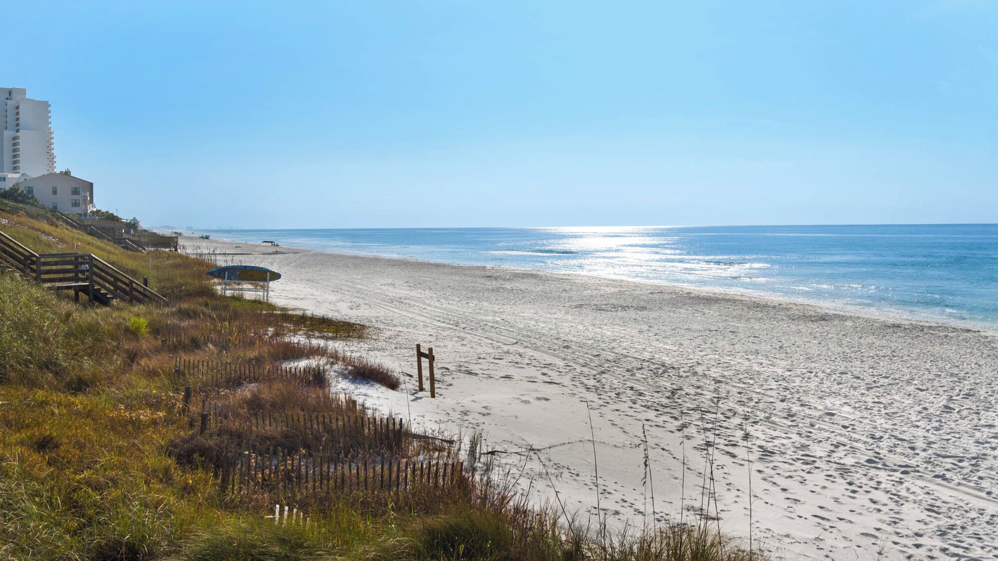 A beach with a wooden staircase leading to a building, a sandy shore, and the ocean.