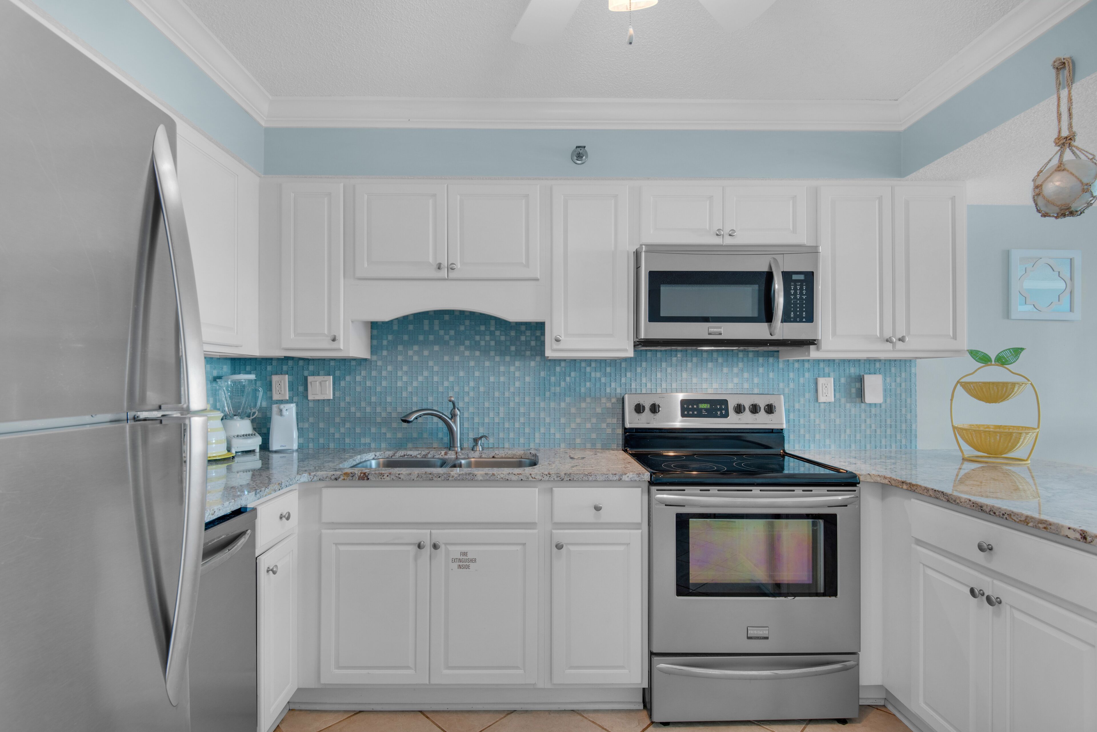 A kitchen with white cabinets, a stainless steel refrigerator, a microwave, an oven, and a sink.