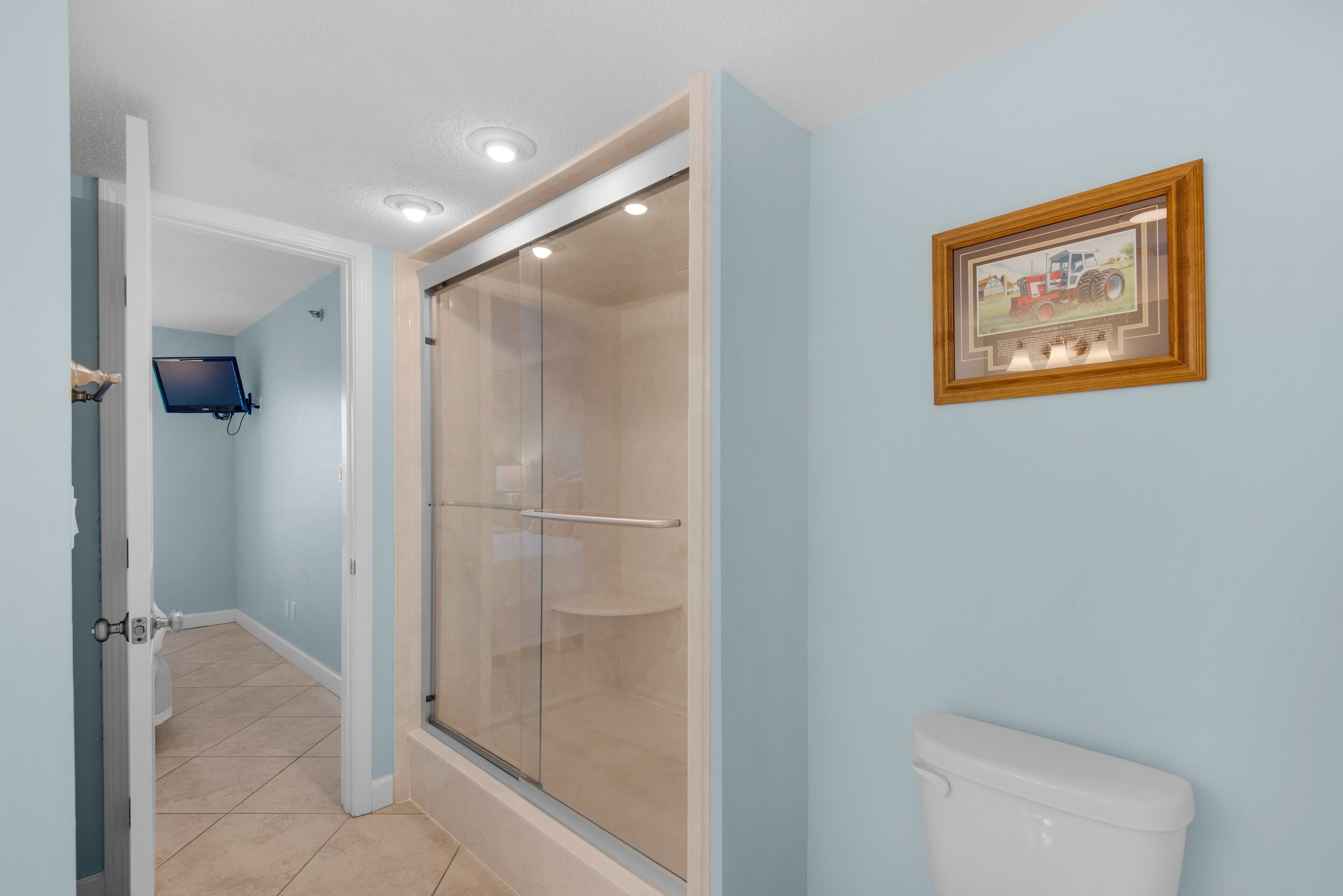 Un bagno con cabina doccia in vetro, un water e un quadro appeso al muro.