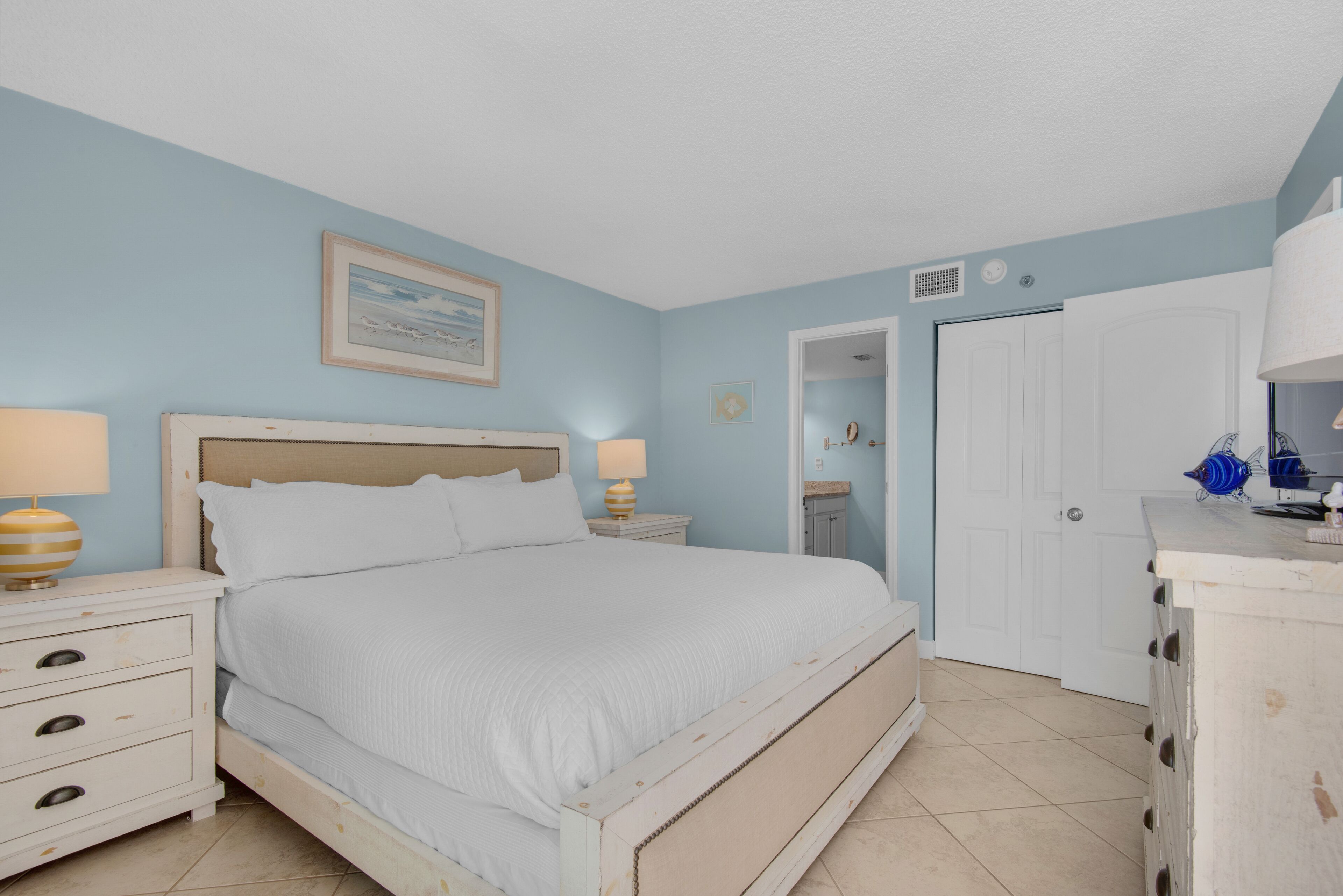 A bedroom with a bed, nightstands, a dresser, and a door leading to another room.