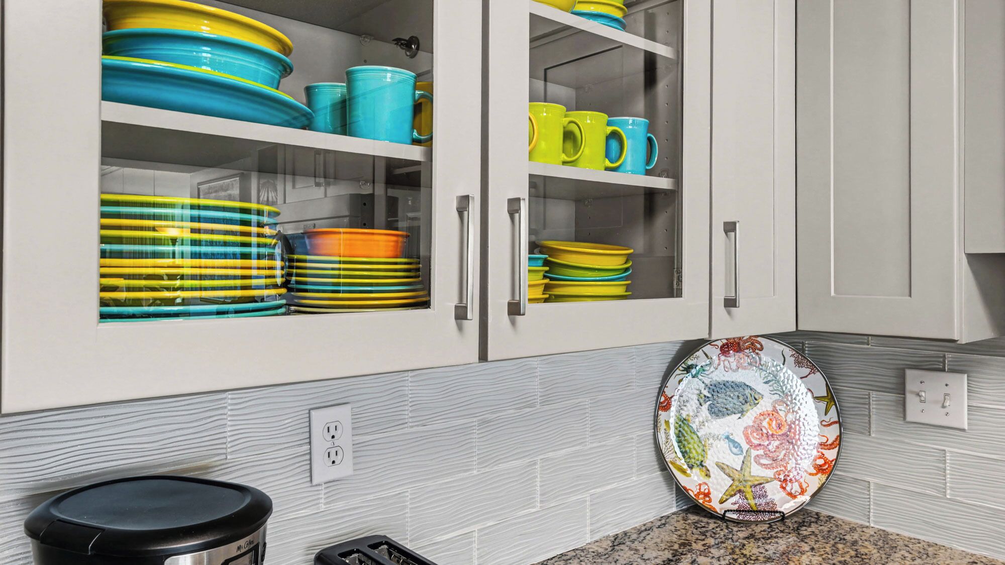 Una cucina con mobili bianchi, piatti colorati e un piatto decorativo sul bancone.