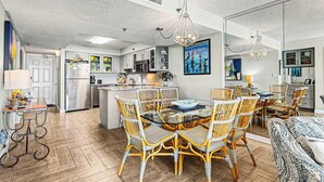 A modern kitchen with white cabinets, a central island, and a dining area with wicker chairs and a glass table.