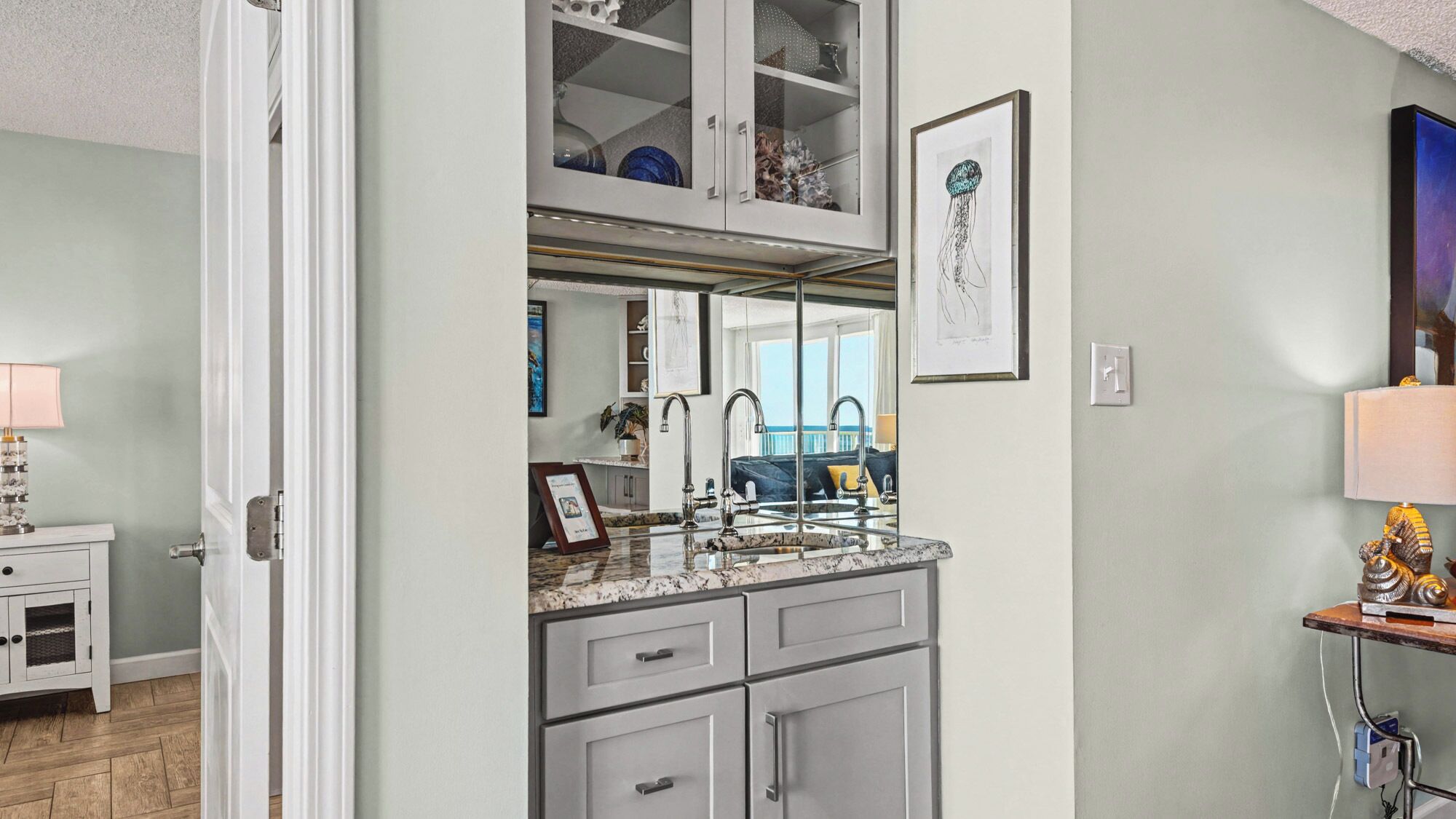 A modern kitchen with a large island, a double sink, and a glass-fronted upper cabinet.