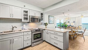 A modern kitchen with grey cabinets, stainless steel appliances, a large island, and a view of the ocean.